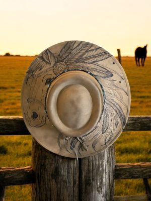 a cowboy hat with a burned image of a horse, hanging on a fencepost